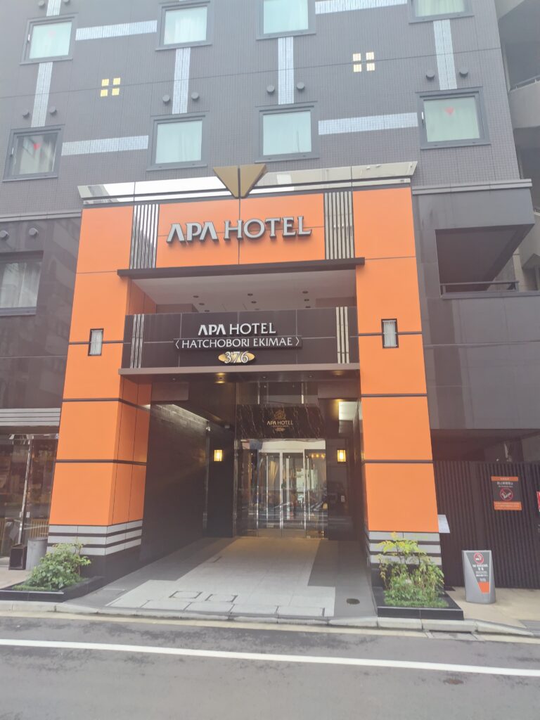 アパホテル〈八丁堀駅前〉のエントランス。オレンジの柱とAPA HOTELの看板